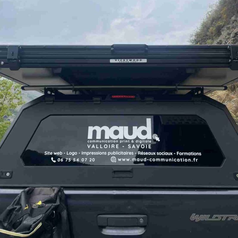 Arrière d’un pick-up Ford Wildtrak avec un sticker noir et blanc présentant les services de Maud Communication à Valloire : création de sites web, logos, impressions publicitaires, réseaux sociaux et formations.
